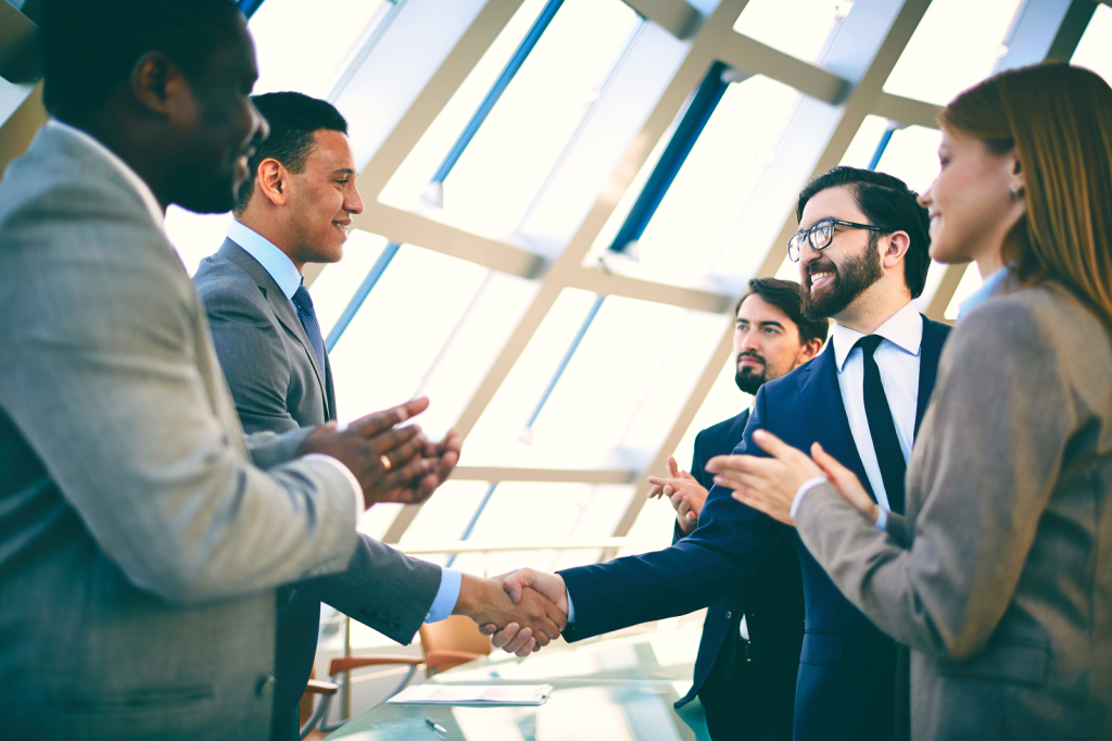 Two successful businessmen handshaking while their colleagues cl